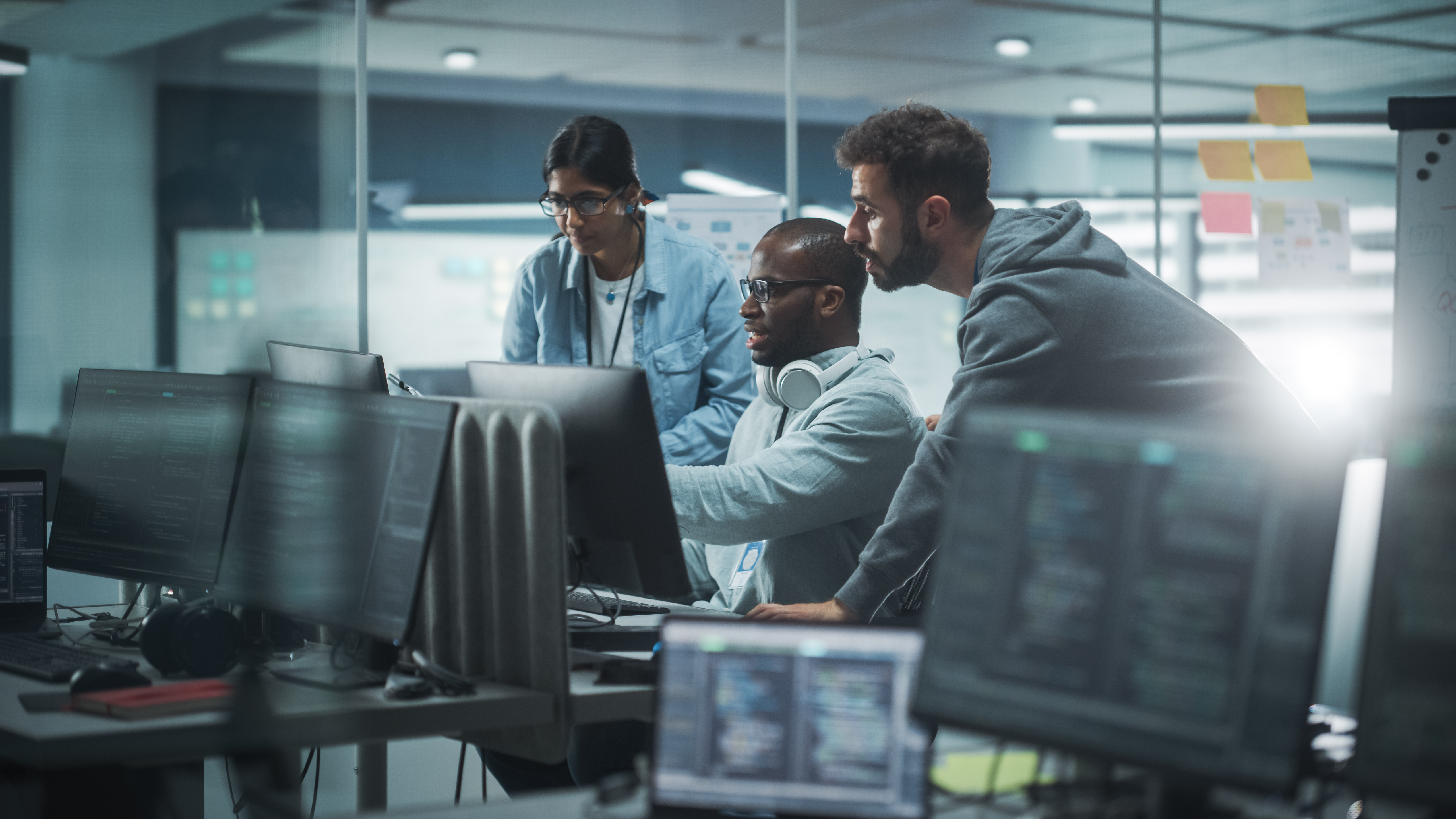 Three colleagues collaborating at computer workstations in a security operations office.